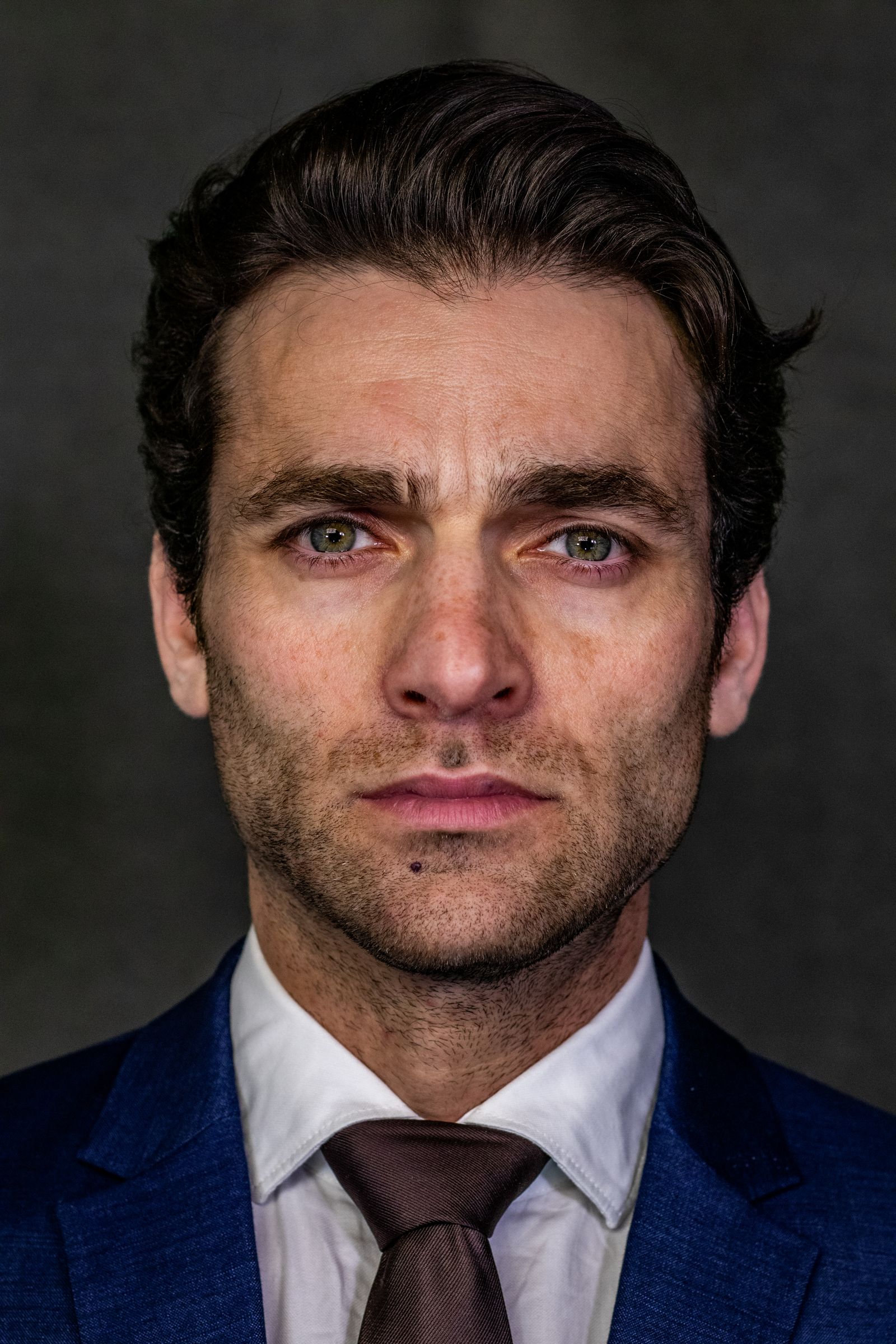 Close-up portrait of a businessman in a blue suit and tie against a gray background.