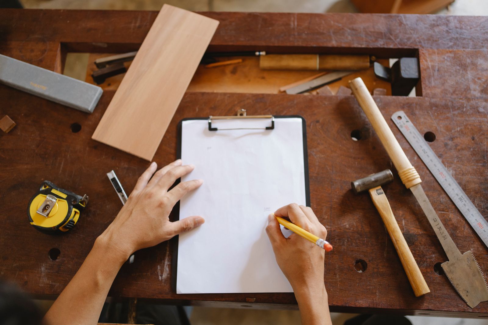 From above of crop faceless man holding pencil and paper while sitting at wooden table with instruments