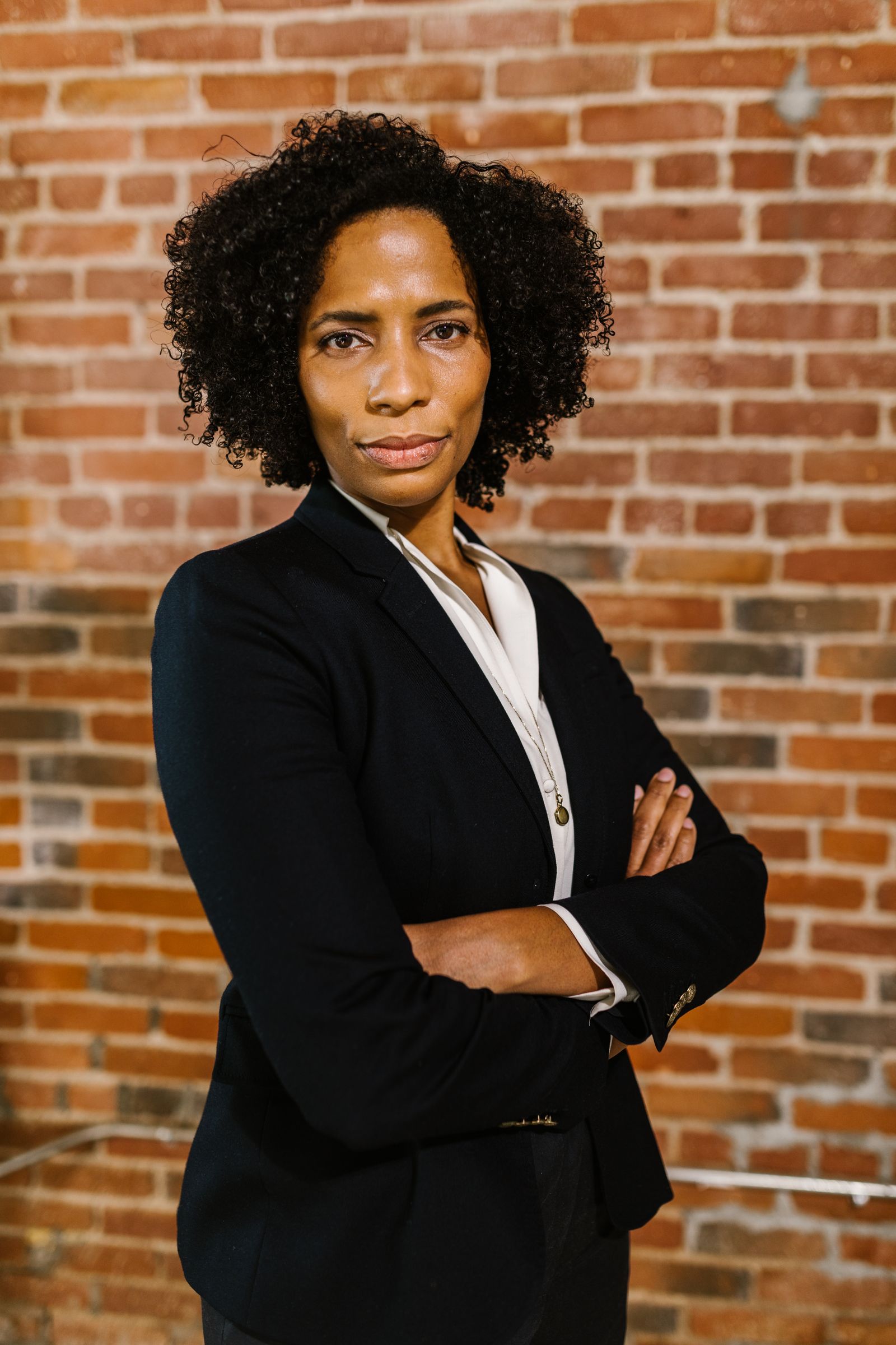 Portrait of a confident businesswoman in formal attire standing against a brick wall background.