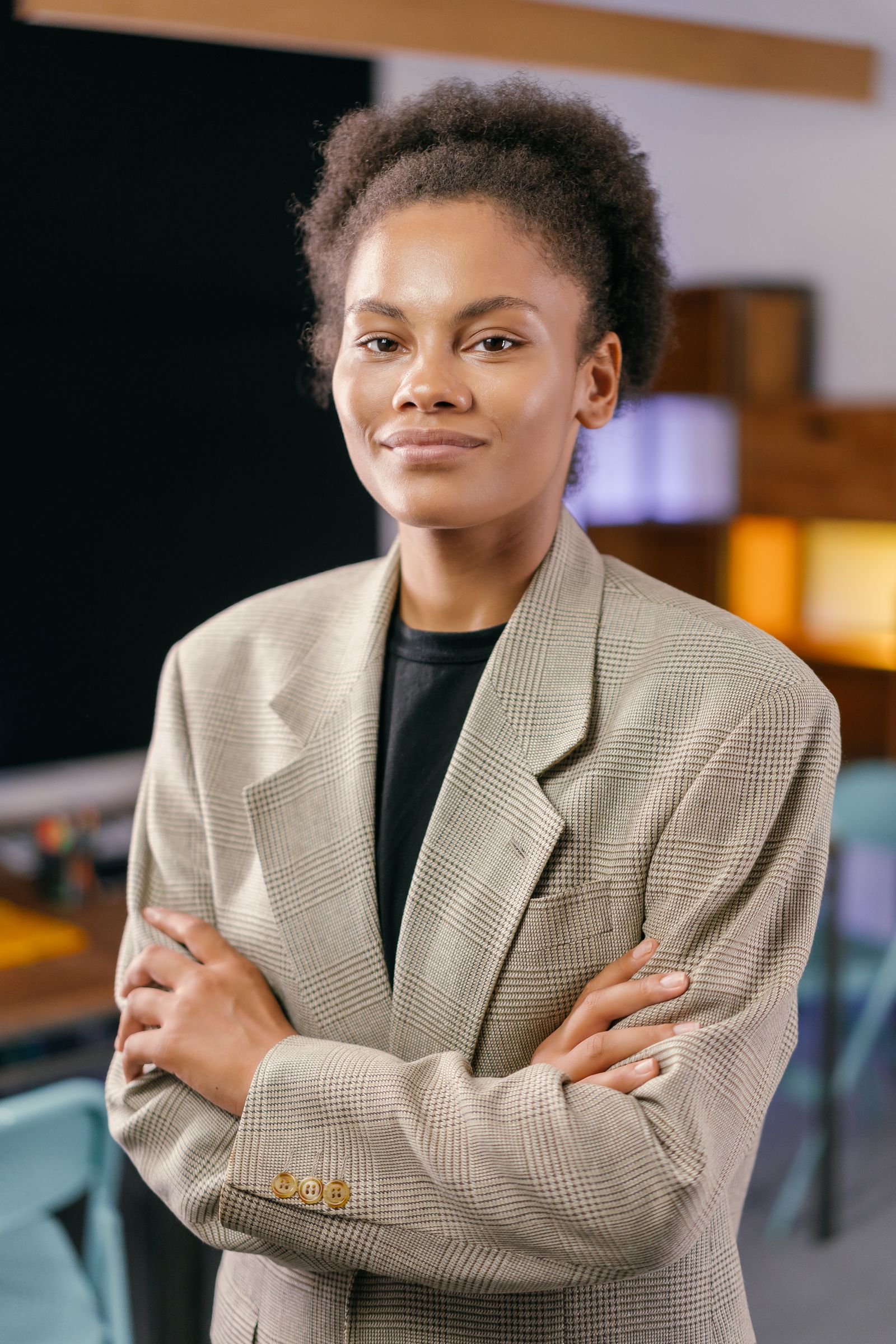 A confident African American businesswoman poses with arms crossed in a modern office setting.